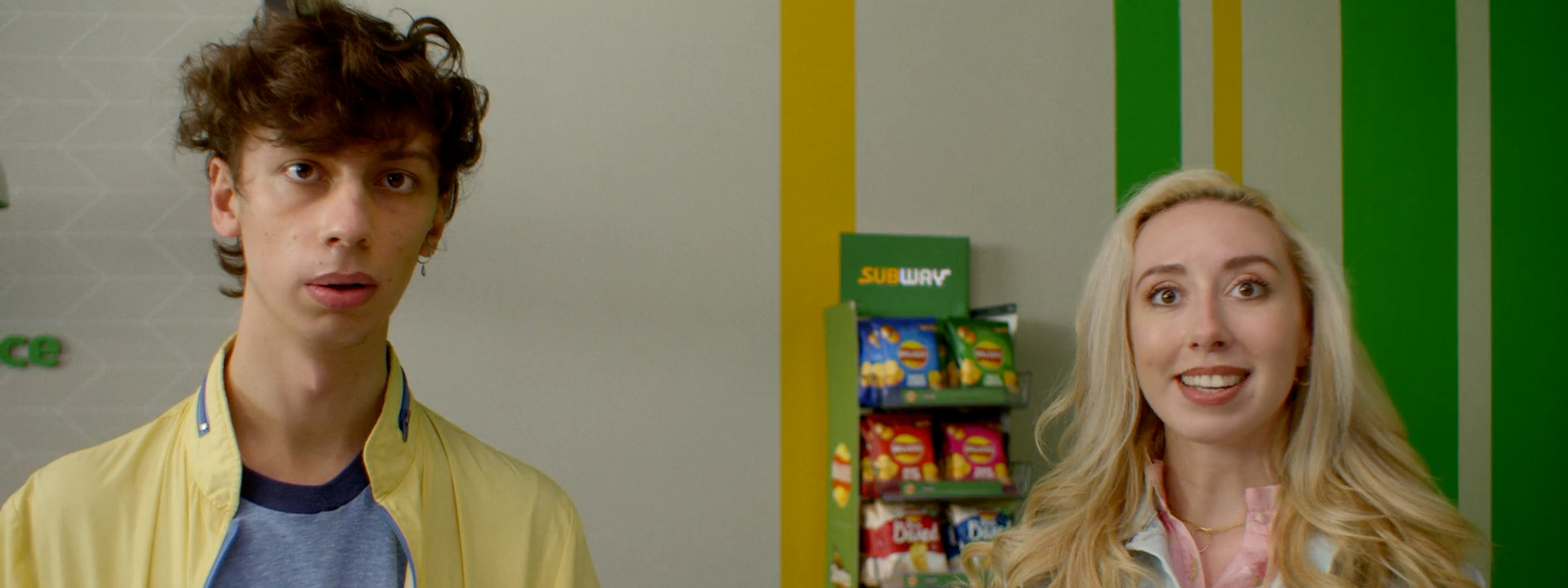 A couple in a Subway fast food restaurant with the Walkers crisps range displayed on a shelf behind them