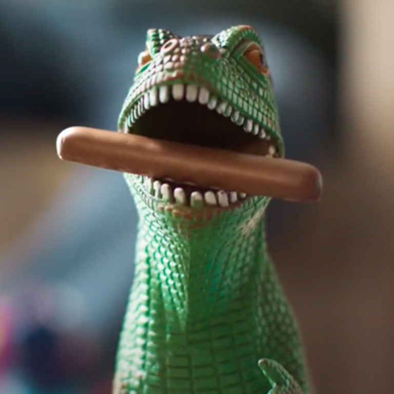 A toy dinosaur with a Cadbury Dairy Milk Finger biscuit in its mouth