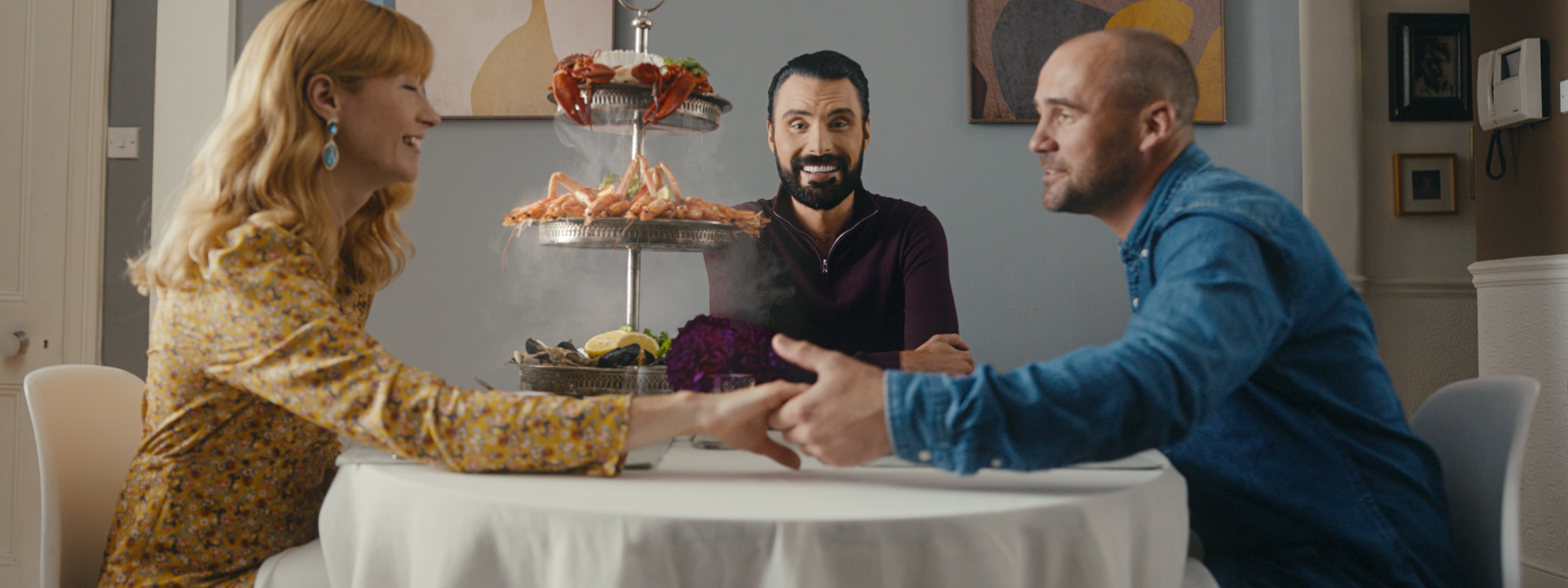 Rylan sits at a table of food with a woman on the left and her date on the right.