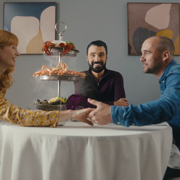 Rylan sits at a table of food with a woman on the left and her date on the right.